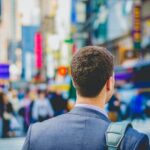 Photo of a man carrying a backpack and walking in Times Square as a featured image for a post about tips for a successful return to work after rehab