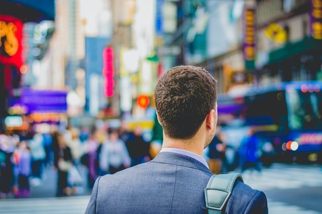 Photo of a man carrying a backpack and walking in Times Square as a featured image for a post about tips for a successful return to work after rehab