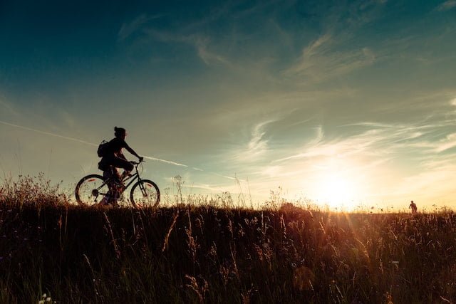 Photo of a person riding a bicycle on a hill during a sunset
