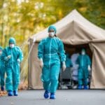 Outdoor Containment Setup with Medical Personnel in Protective Gear Walking Towards Tent During Autumn Season in a Forest Environment