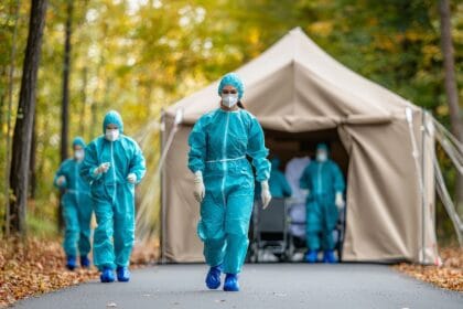 Outdoor Containment Setup with Medical Personnel in Protective Gear Walking Towards Tent During Autumn Season in a Forest Environment